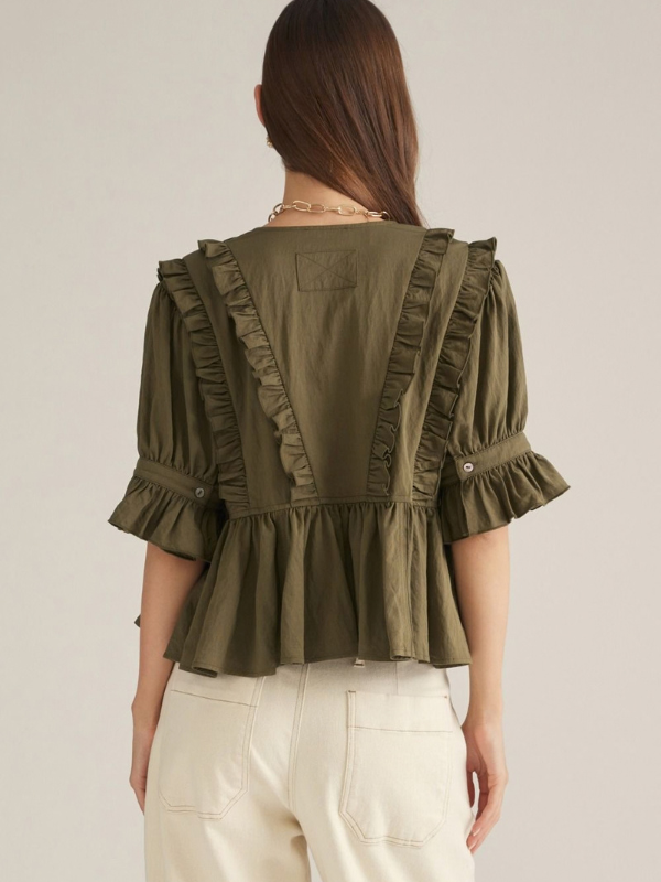 woman wearing an olive v neck ruffle top and ecru pants