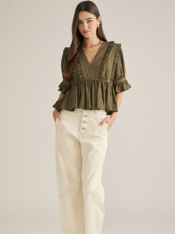 woman wearing an olive v neck ruffle top and ecru pants
