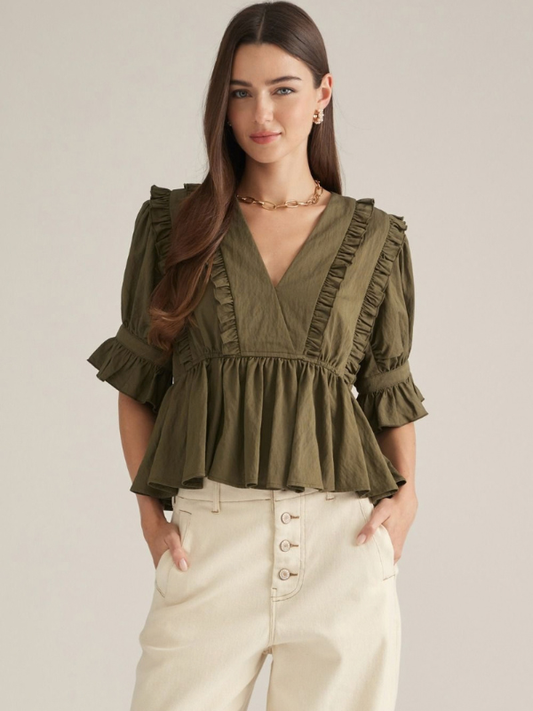 woman wearing an olive v neck ruffle top and ecru pants