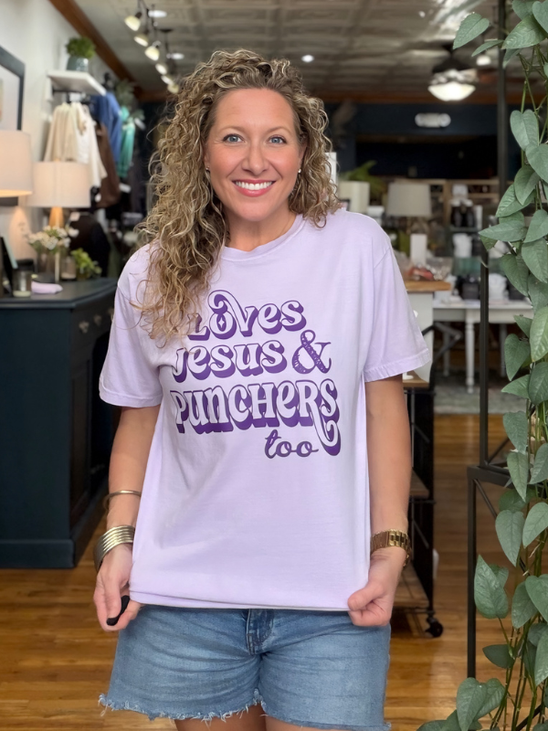 woman wearing a lavender tee that says Loves Jesus & The Punchers too in dark purple ink 