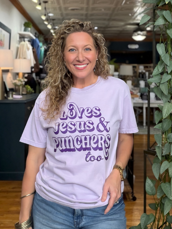 woman wearing a lavender tee that says Loves Jesus & The Punchers too in dark purple ink 
