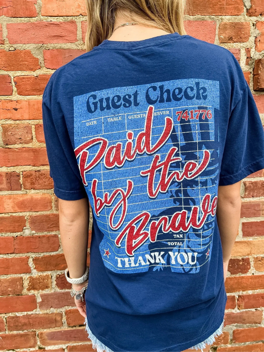Person wearing a blue t-shirt with text and graphics against a brick wall.