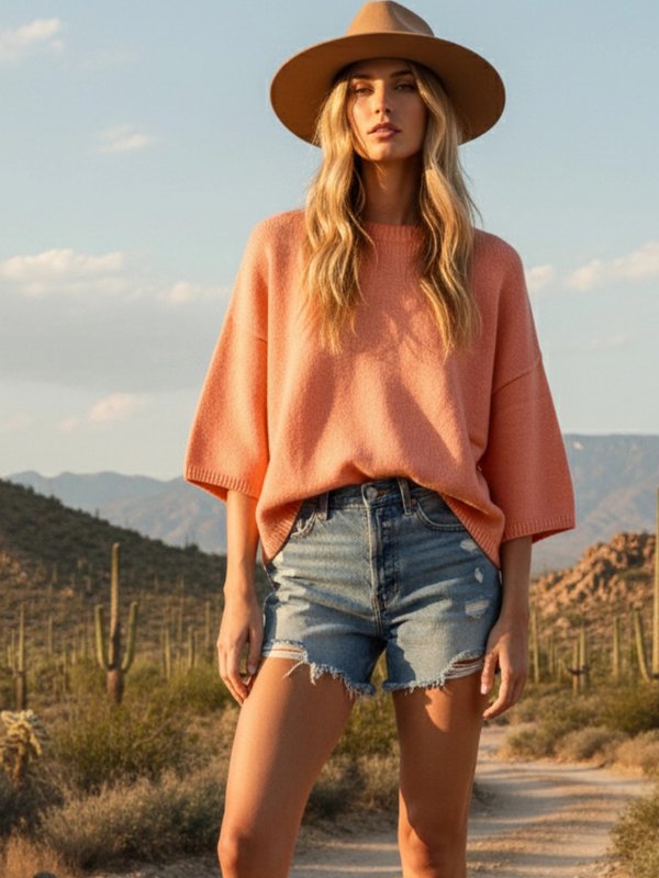Woman in a pink sweater and denim shorts standing in a desert landscape
