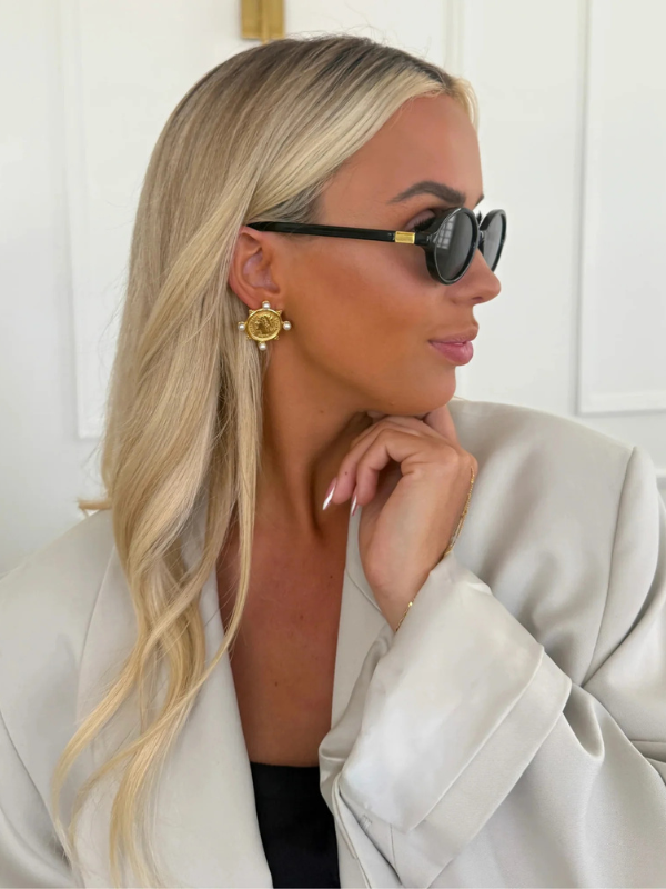 Woman wearing sunglasses and a light-colored blazer with a neutral background