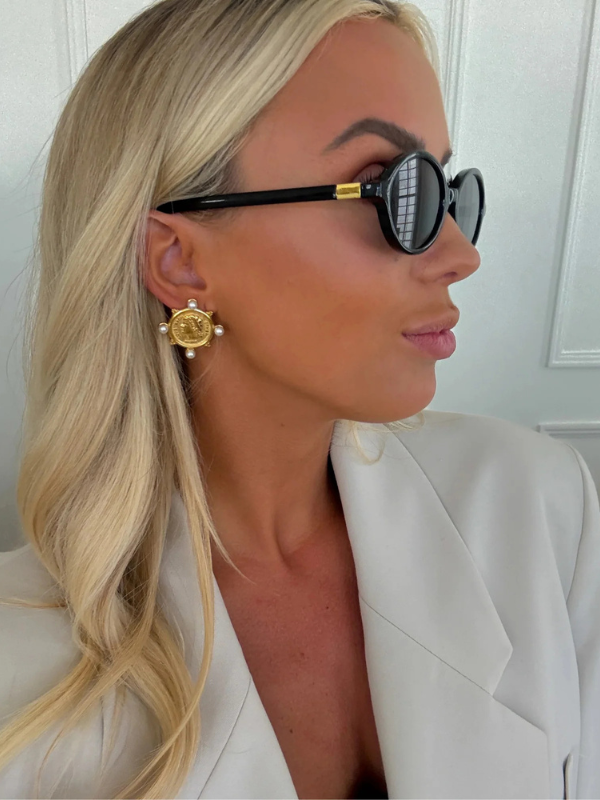 Woman wearing black sunglasses and gold earrings with a white background