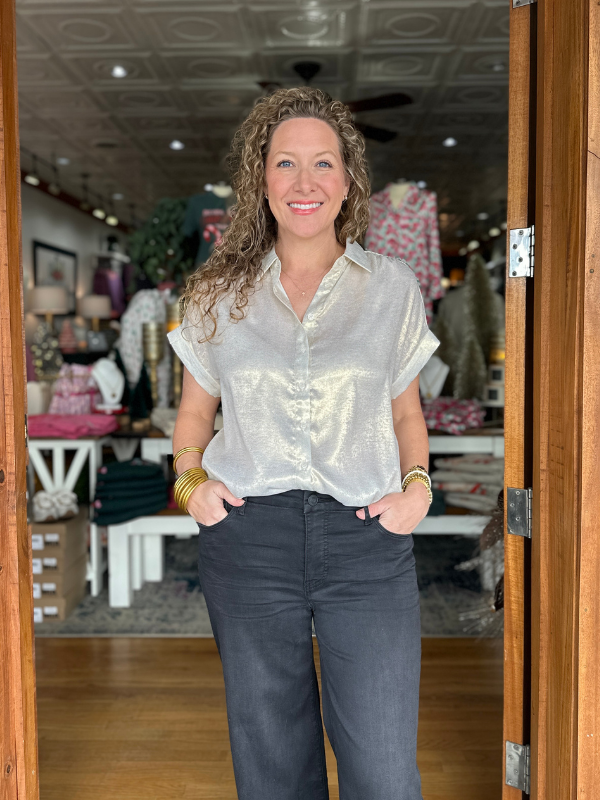 Woman standing in a store doorway wearing a light-colored shirt and dark pants.