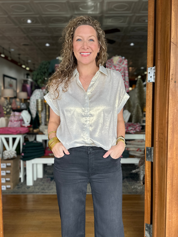 Woman standing in a store wearing a light-colored blouse and dark jeans.