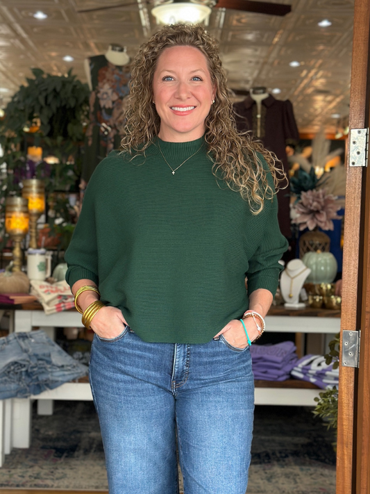 Woman wearing a green sweater and blue jeans standing in a store.