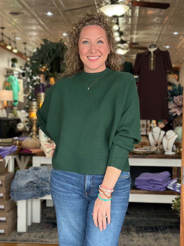 Woman wearing a green sweater and blue jeans standing in a store.