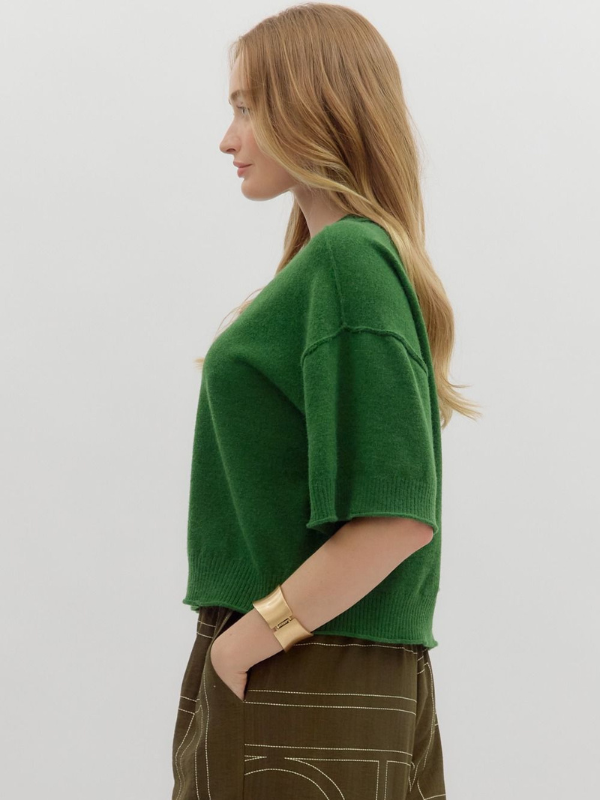 Woman wearing a green sweater and brown pants against a white background