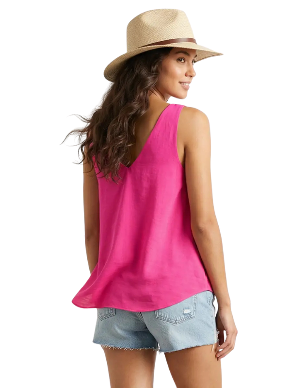 A woman wearing a bright pink sleeveless tank top, light blue denim shorts, and a beige straw hat, shown from a back-three-quarter view against a plain white background.