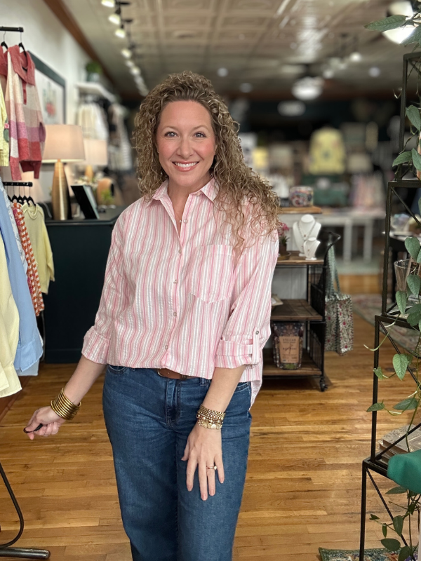 Woman in a striped shirt and jeans standing in a store with wooden floors and clothing racks.