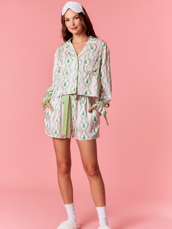 Woman wearing a patterned pajama set with shorts on a pink background