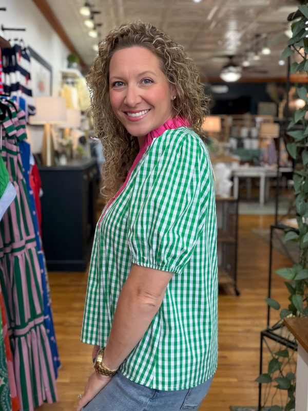 Woman in a green checkered shirt standing in a store with clothing racks and decor.