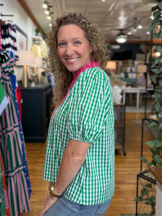 Woman in a green checkered shirt standing in a store with clothing racks and decor.