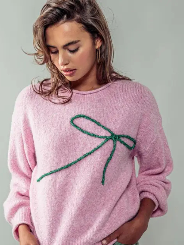 Woman wearing a pink sweater with a green bow design on a plain background