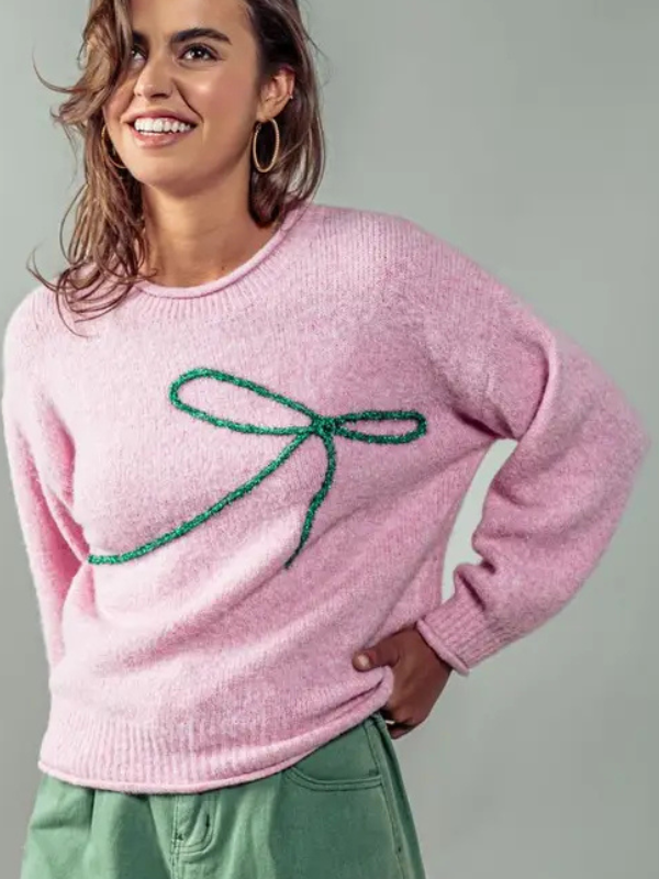 Woman wearing a pink sweater with a green bow design on a gray background