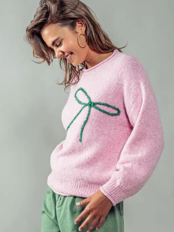 Woman wearing a pink sweater with a green bow design on a gray background