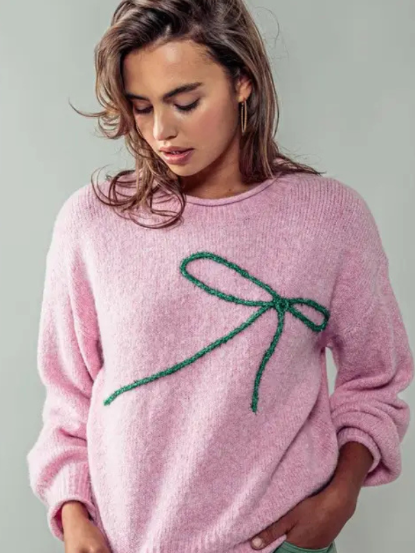 Woman wearing a pink sweater with a green bow design on a plain background