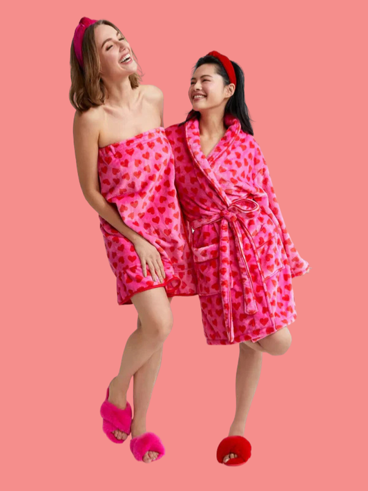 Two women wearing pink heart-patterned robes on a pink background