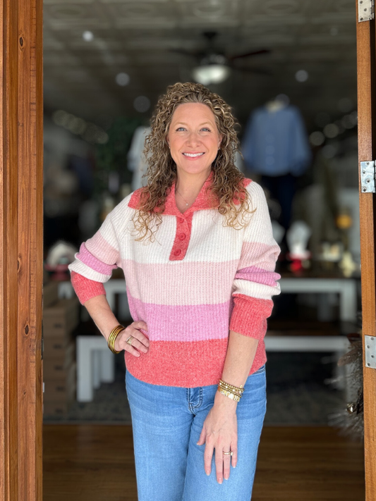 Woman wearing a colorful striped sweater and blue jeans standing in a doorway.