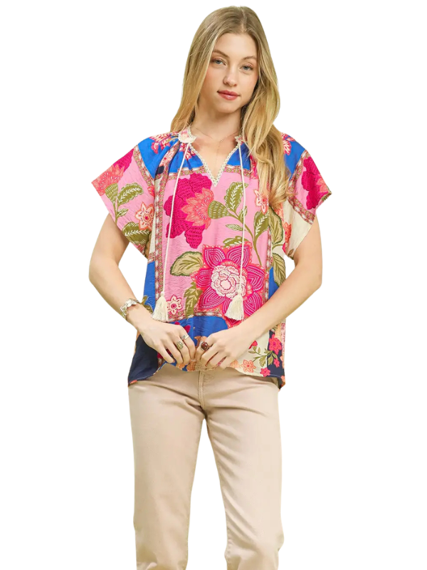 A woman modeling a short-sleeve floral top with a drawstring neckline, paired with beige pants, against a plain white background.