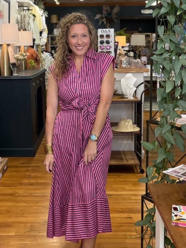 Woman in a purple striped dress standing in a store with various items on shelves.