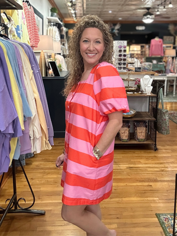 Woman wearing a red and pink striped dress in a clothing store.
