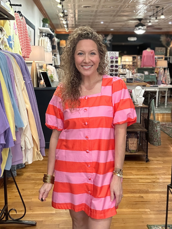 Woman wearing a red and pink striped dress in a clothing store.