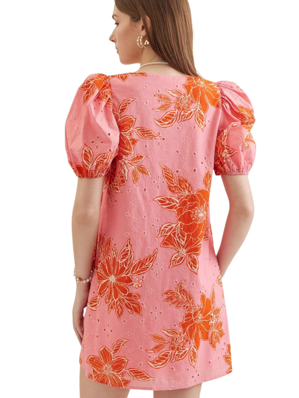Woman wearing a pink dress with orange floral patterns on a white background