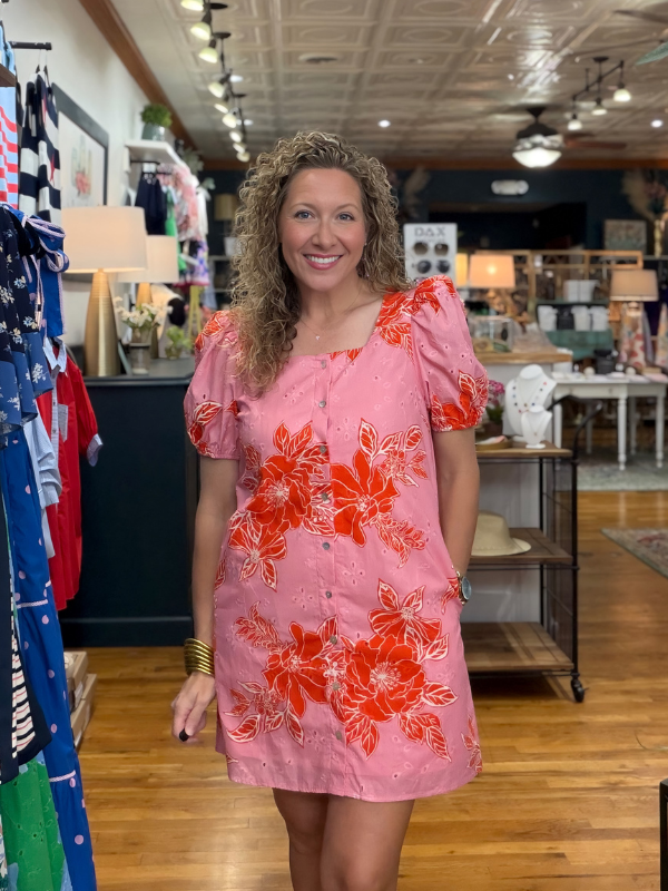 Woman wearing a pink dress with orange floral patterns in a store setting.