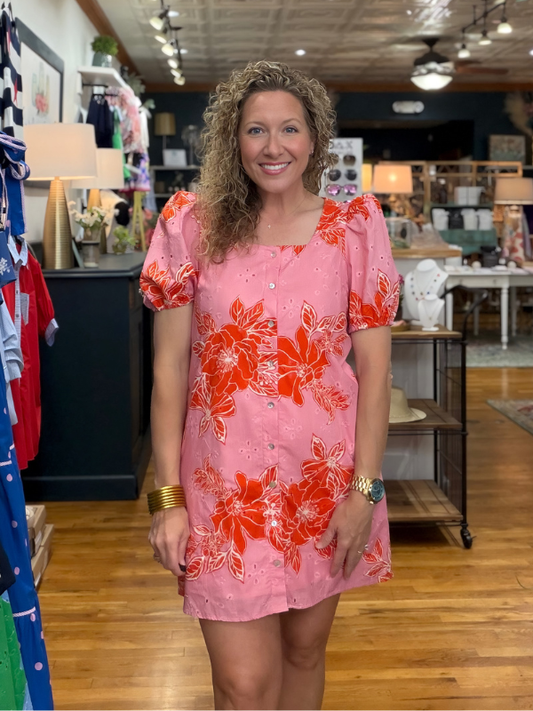 Woman wearing a pink dress with red floral pattern in a store setting