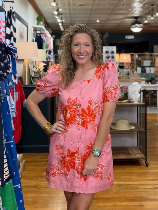 Woman wearing a pink dress with orange floral patterns in a store setting.