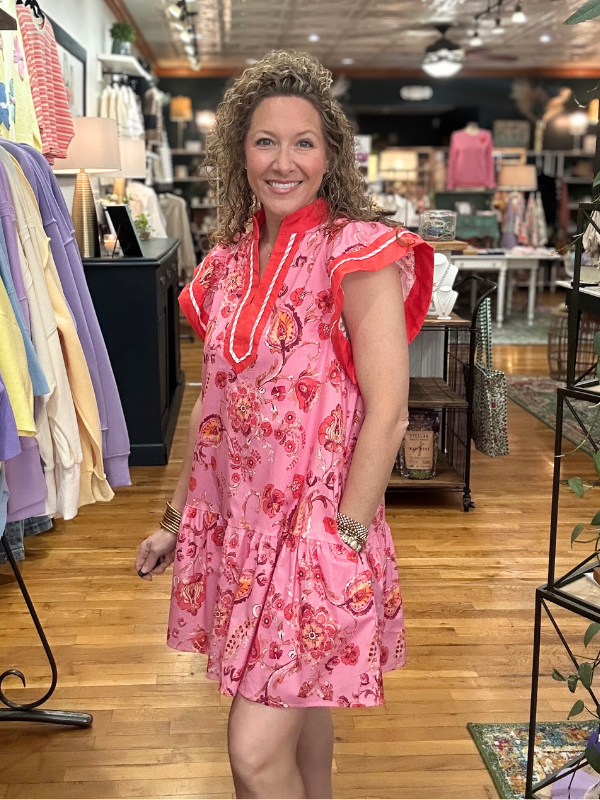 Woman in a pink dress standing in a store with racks of clothes in the background.