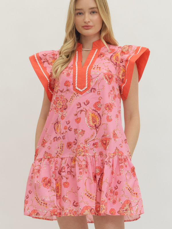 Woman wearing a pink floral dress with orange accents on a plain background