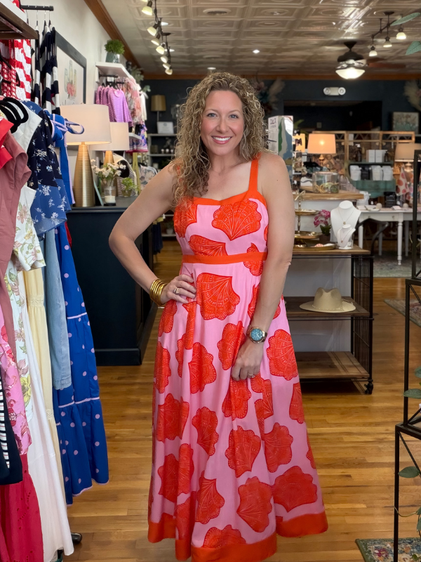Woman in a red and pink floral dress standing in a store with clothing racks.