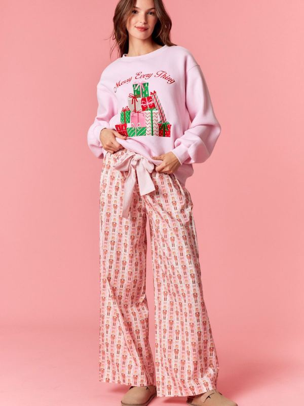 Woman wearing a pink sweatshirt with a Christmas tree design and wide-leg pants on a pink background