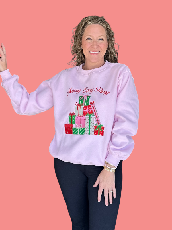 Woman wearing a pink sweatshirt with Christmas-themed design on a pink background