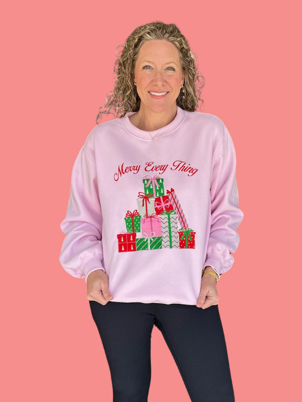 Woman wearing a pink sweatshirt with Christmas-themed design and text on a pink background