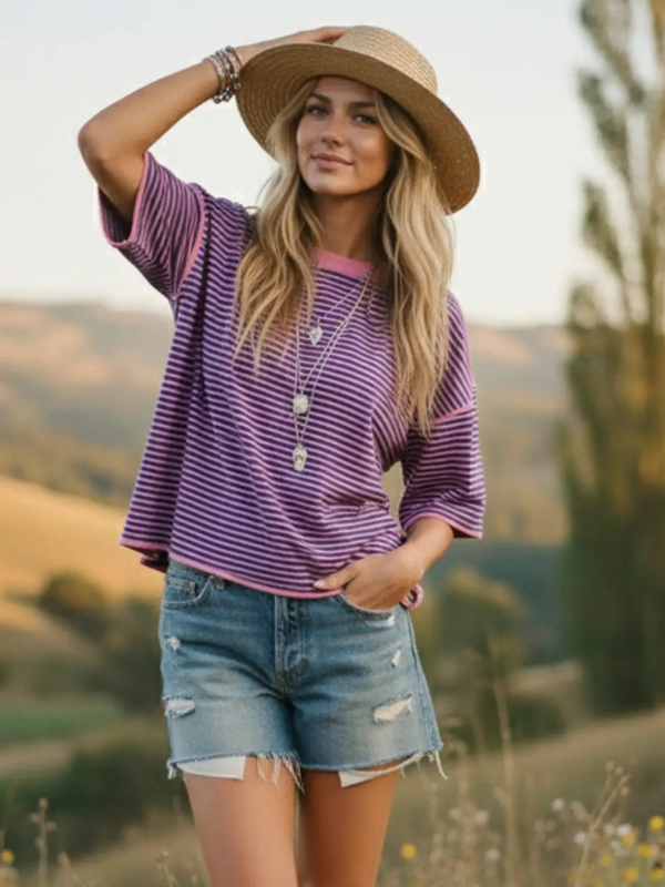 Woman wearing a purple striped shirt, denim shorts, and a straw hat in a scenic outdoor setting.