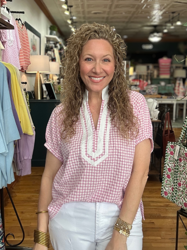 Woman wearing a pink checkered shirt with white trim in a store setting