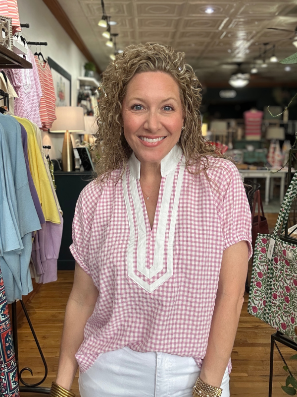 Woman wearing a pink checkered blouse with a white scarf in a clothing store.