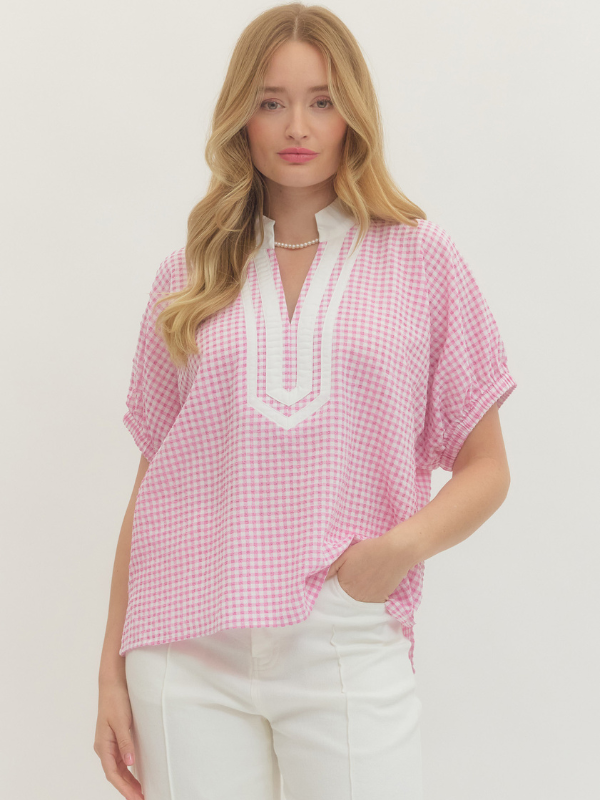 Woman wearing a pink checkered blouse with white trim on a plain background
