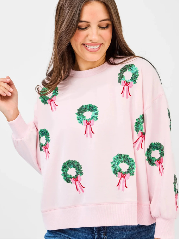 Woman wearing a pink sweater with green wreath patterns on a white background