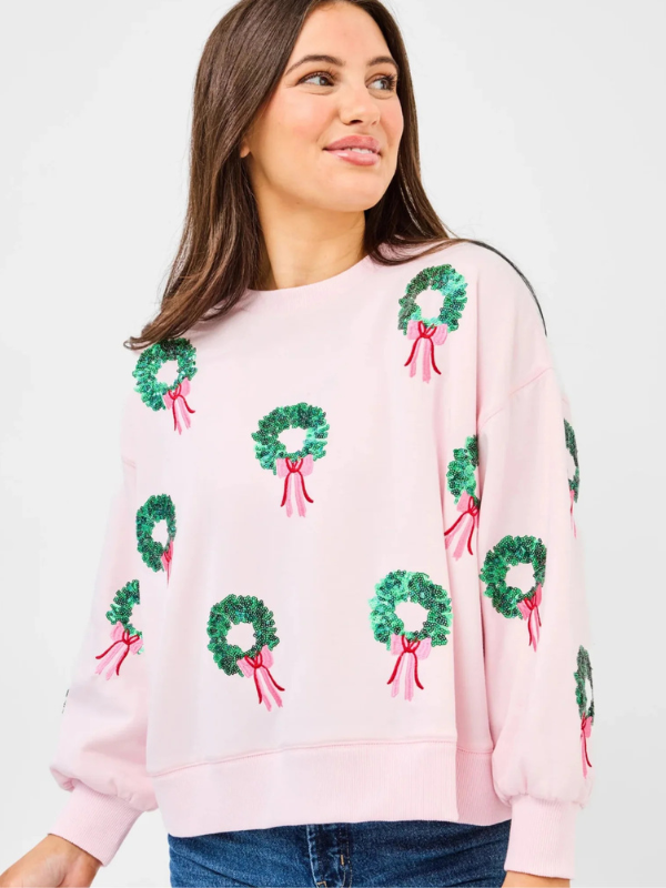 Woman wearing a pink sweater with green wreath patterns on a white background