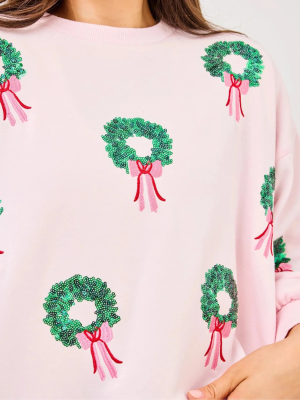 Close-up of a pink sweater with green wreath and pink bow designs.