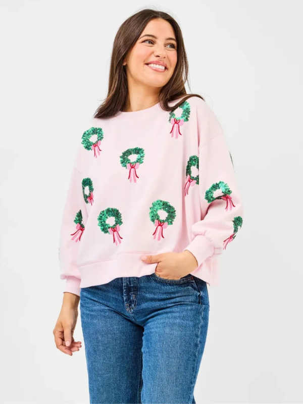 Woman wearing a pink sweater with green wreath patterns on a white background