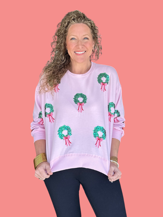 Woman wearing a pink sweater with green wreath patterns on a coral background