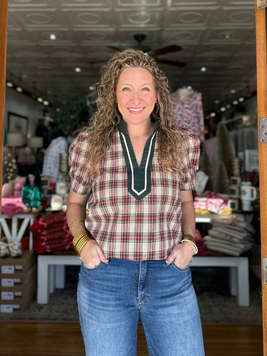 Woman wearing a plaid shirt and jeans standing in a store with various items in the background.