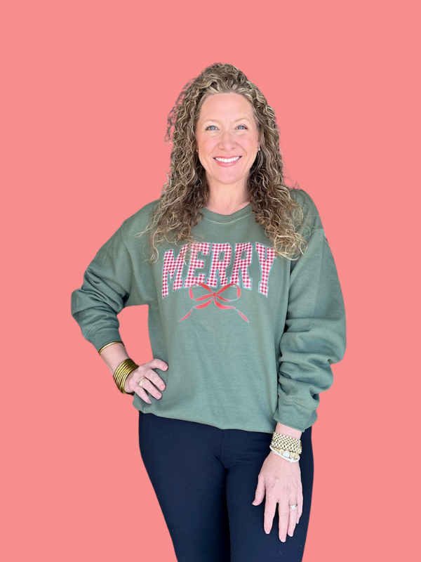Woman wearing a green sweatshirt with 'MERRY' text on a pink background
